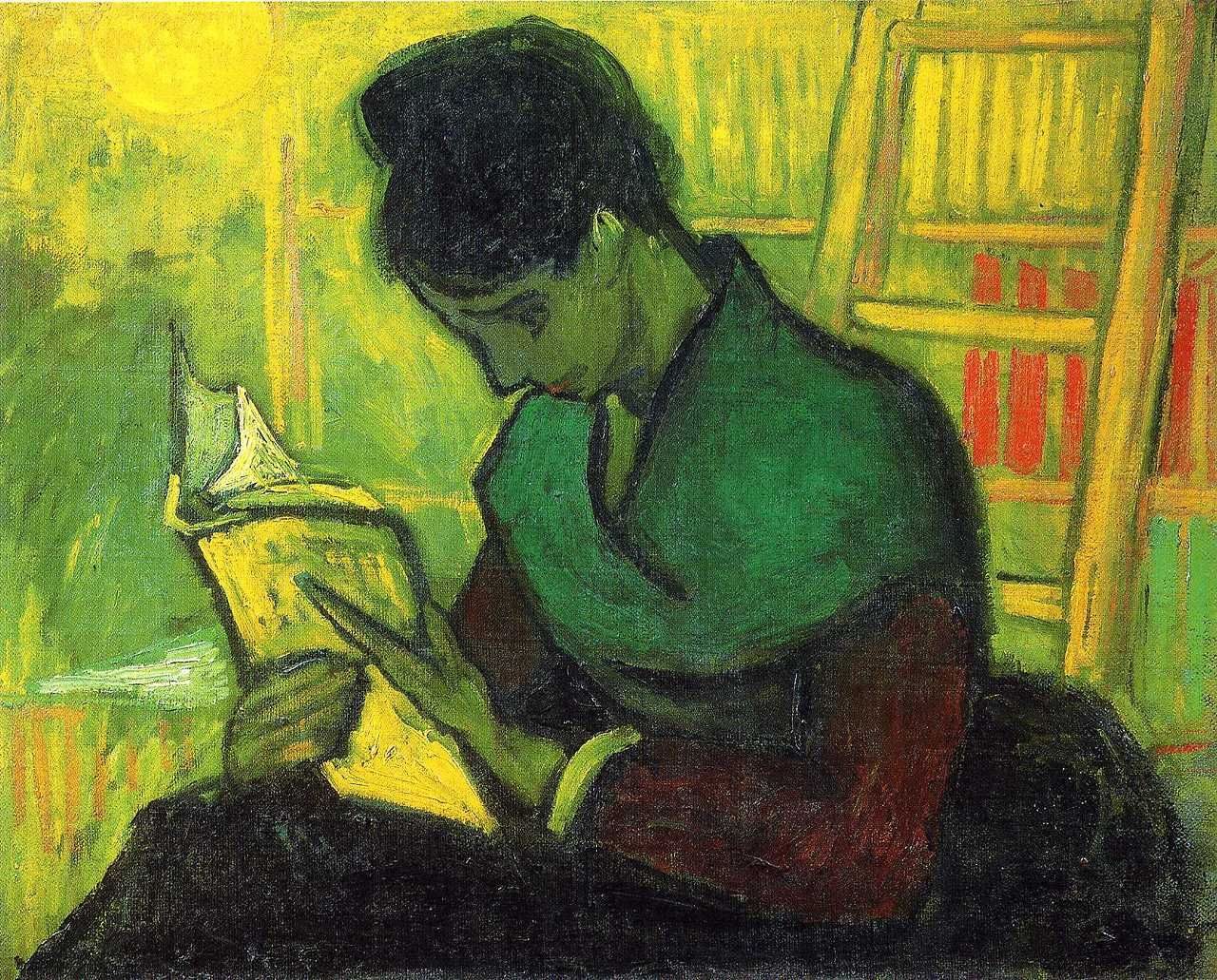 Una mujer está sentada junto a una estantería y se inclina con atención sobre el libro que está leyendo.